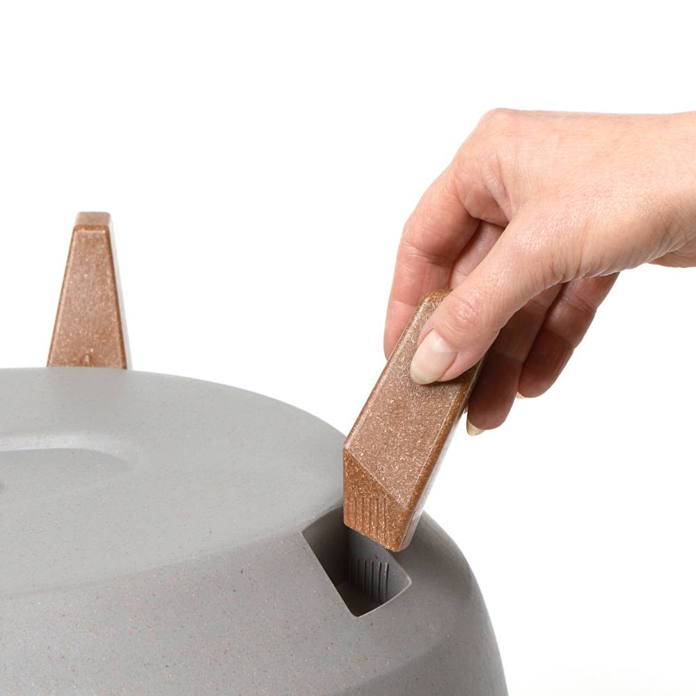 Dłoń trzyma brązowy drewniany klocek nad szarym obiektem z otworami, gotowa do włożenia.