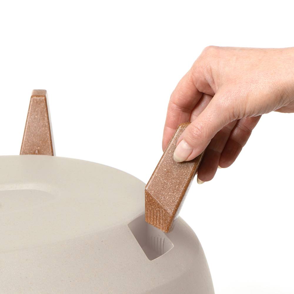 Ręka wkłada prostokątny drewniany przedmiot do szczeliny okrągłego, kremowego obiektu.