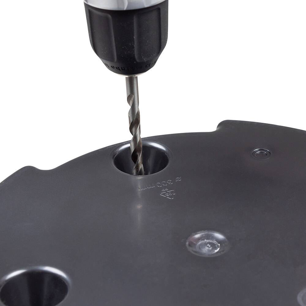 Wiertło przenika przez okrągłą czarną płytę z tworzywa sztucznego z wieloma otworami.