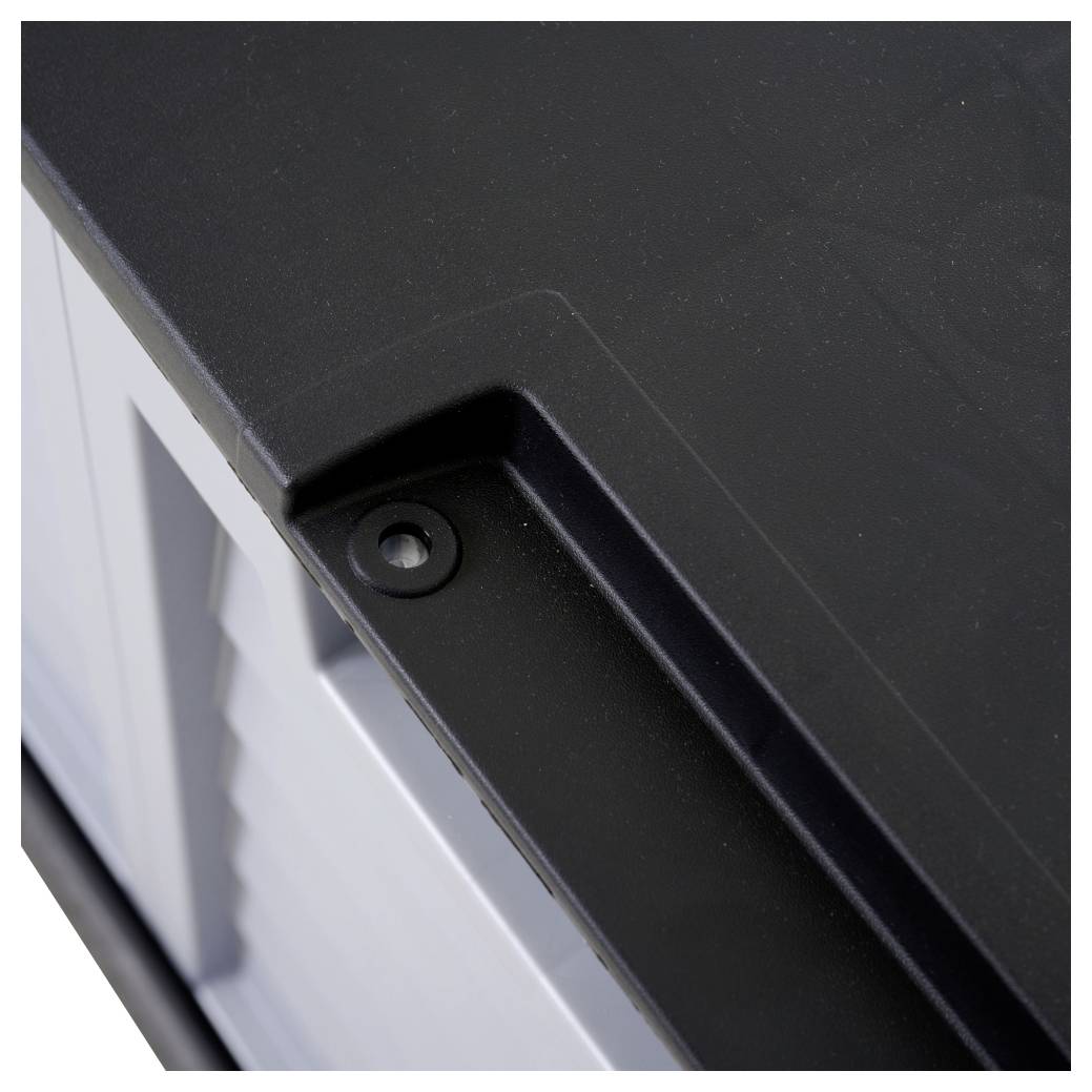 Zbliżenie ciemnej plastikowej pokrywy na pudełku. Pokrywa ma ścięte krawędzie i jest przytrzymywana przez śrubę.