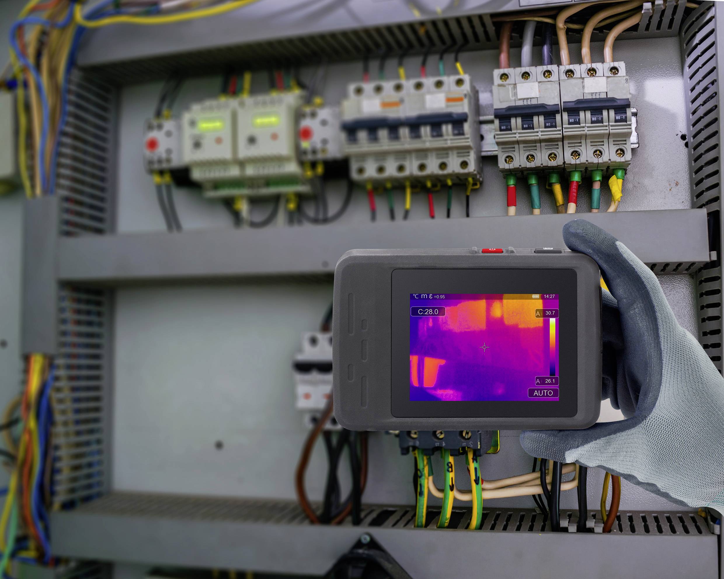 Technik trzyma kamerę termowizyjną przed otwartą szafą sterowniczą i sprawdza komponenty elektryczne pod kątem przegrzania.