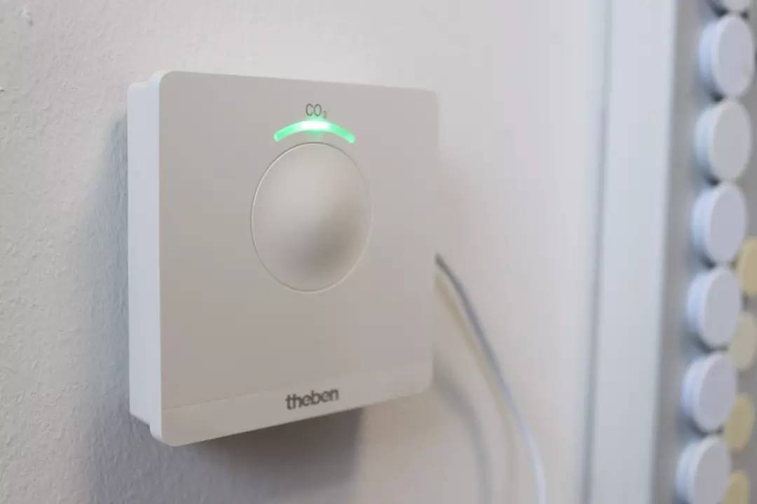 Czujnik CO2 na ścianie, wyświetlający jakość powietrza. Zielone światło wskazuje na normalne poziomy CO2.