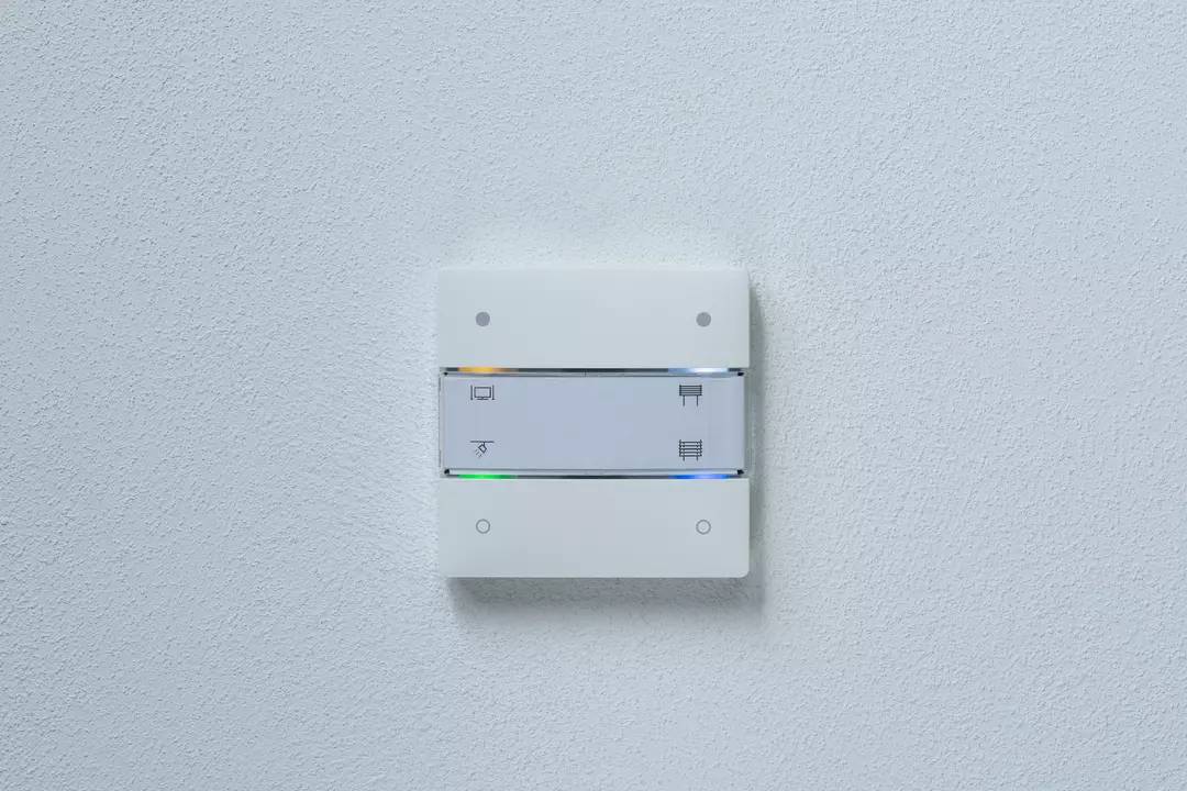 Biały przełącznik z dwoma przyciskami na ścianie, każdy oznaczony symbolami światła i żaluzji.