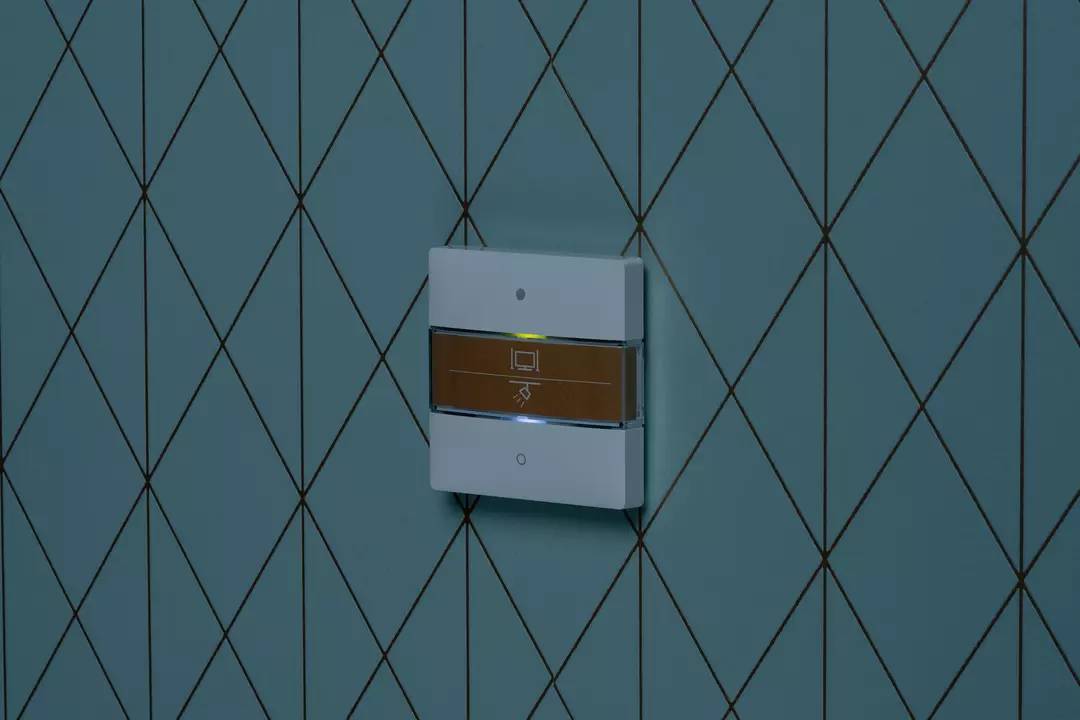 Włącznik światła z subtelnym żółtym światłem w pomieszczeniu o niebieskim wzorze. Symbolizuje nowoczesną technologię i stylowy design.