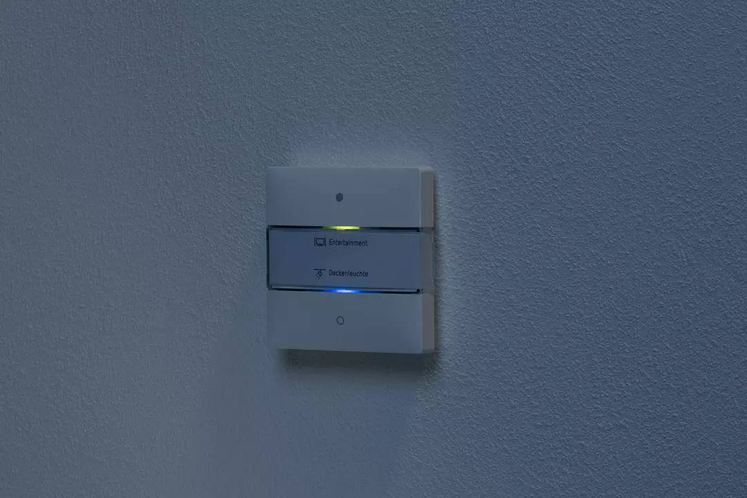 Przełącznik naścienny z dwoma przyciskami, jeden żółty podświetlony z napisem 'Odpowietrzanie', drugi niebieski podświetlony z napisem 'Lampa sufitowa'.