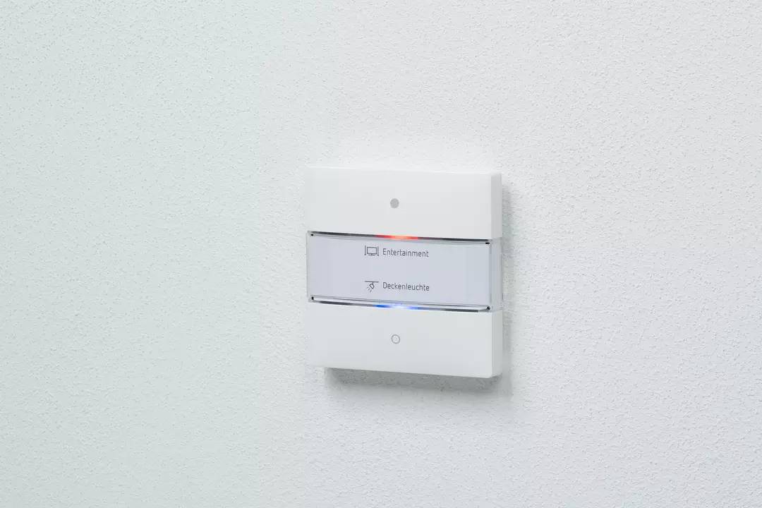 Biały przełącznik na ścianie z dwoma przyciskami: górny 'Rozrywka' z symbolem, dolny 'Oświetlenie sufitowe' z symbolem.