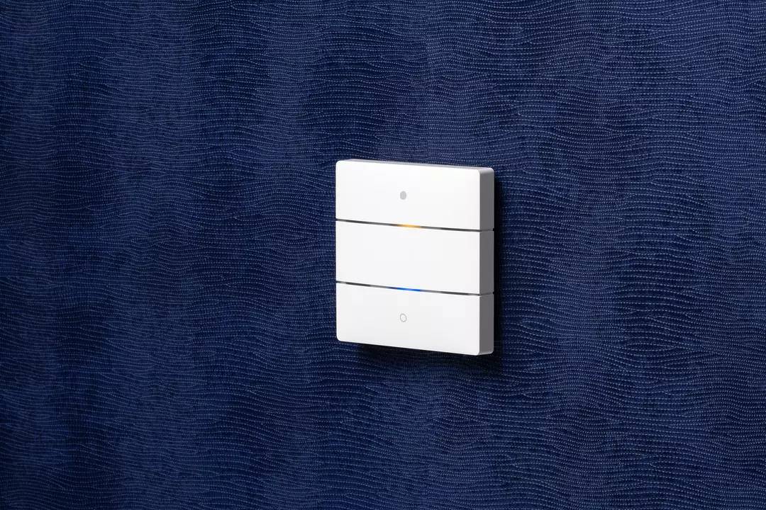 Pojedynczy biały włącznik z trzema przyciskami jest zamontowany na strukturalnej, ciemnoniebieskiej ścianie.