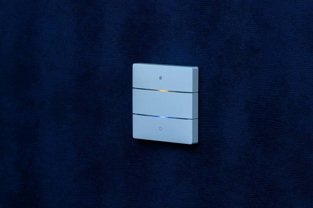 Potrójny włącznik światła na ciemnoniebieskiej ścianie, z świecącym żółtym wskaźnikiem pośrodku.