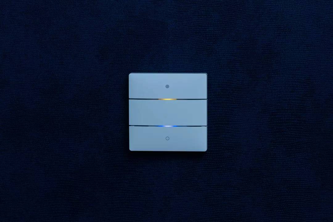 Potrójny włącznik światła na niebieskiej ścianie, z dwoma przełącznikami oznaczonymi małymi świecącymi punktami.