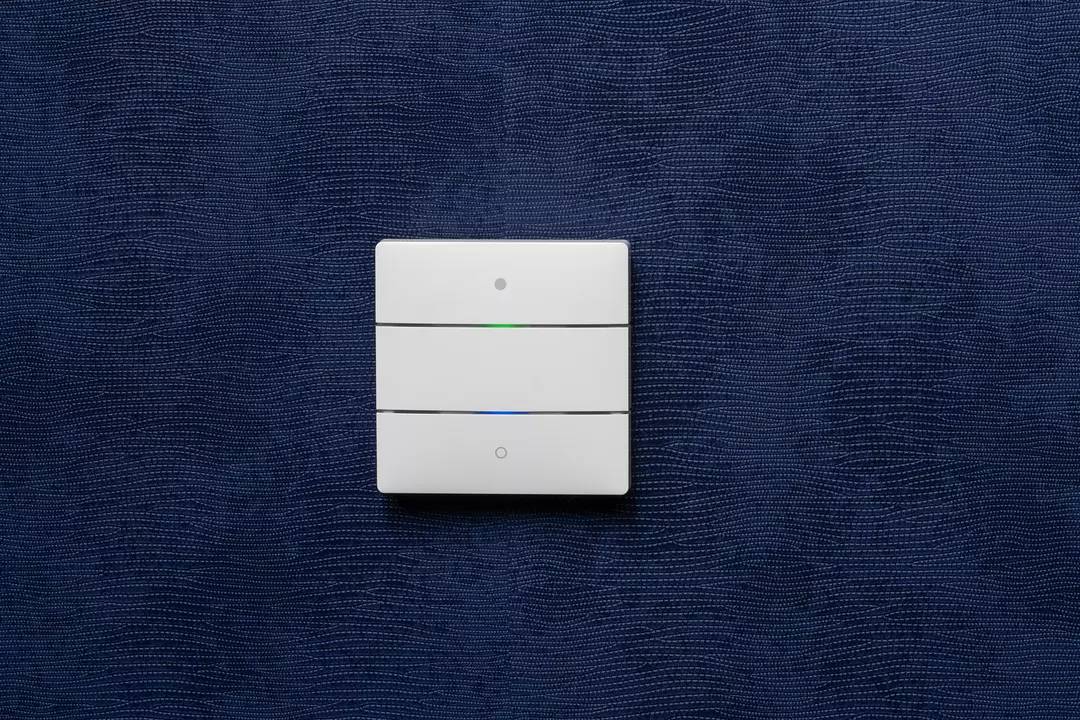 Potrójny włącznik światła z białymi przyciskami jest zamontowany na ciemnoniebieskiej strukturalnej ścianie.