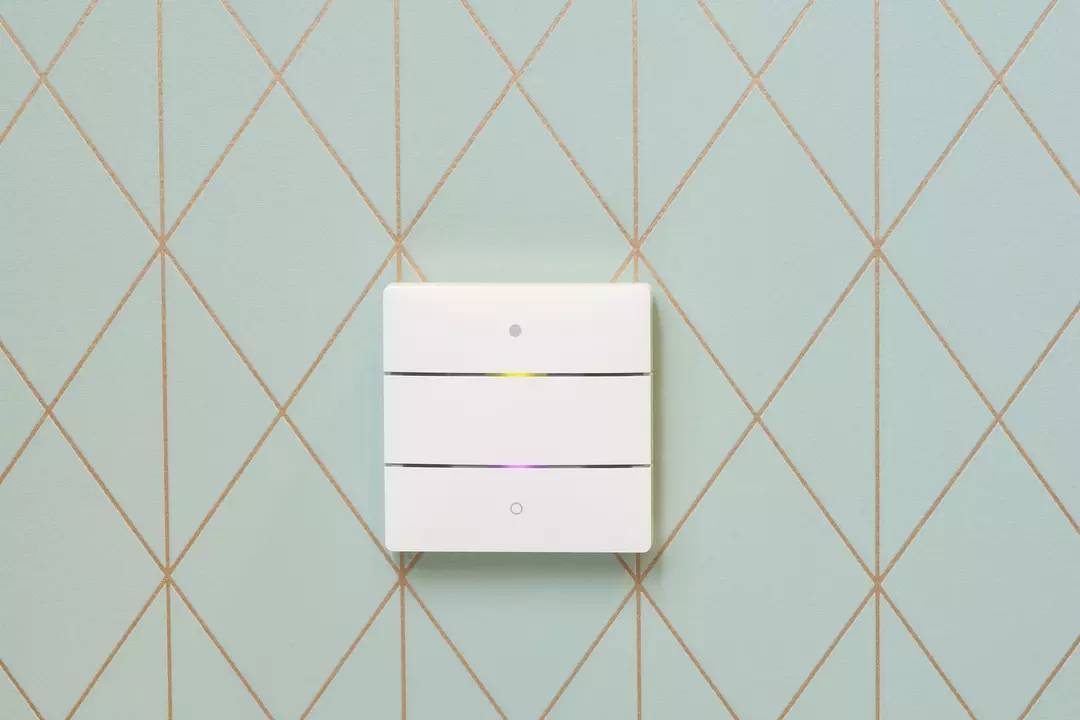 Biały włącznik światła z trzema poziomymi przełącznikami na jasnozielonej ścianie o wzorze rombu.