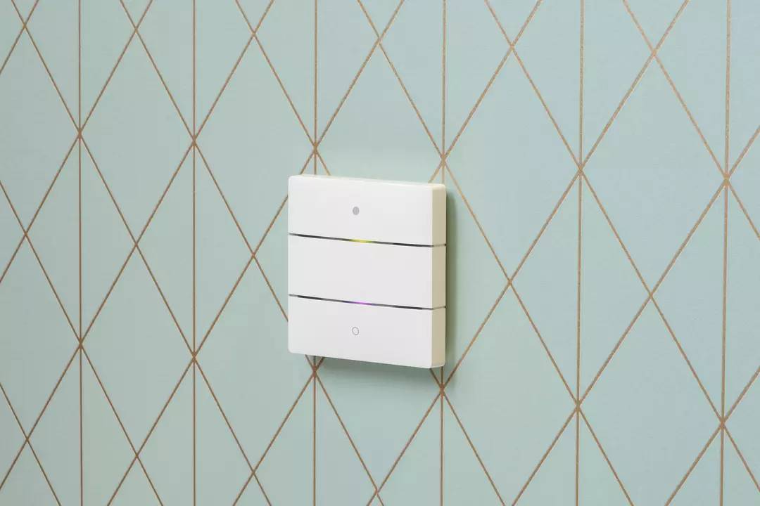 Nowoczesny, trójczęściowy włącznik światła zainstalowany na jasnoniebieskiej ścianie ozdobionej złotymi liniami, nie wykazuje żadnej aktywności.