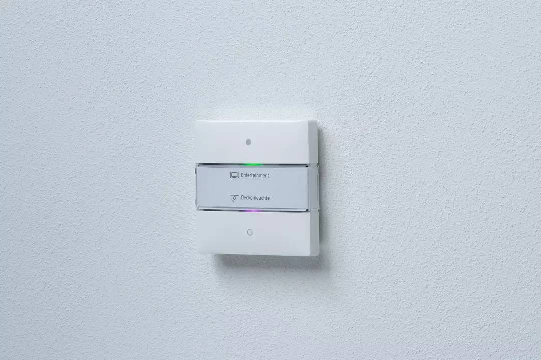 Przełącznik naścienny z dwoma przyciskami, górny dla 'Rozrywki', dolny dla 'Lampy sufitowej', zamontowany na białej ścianie.