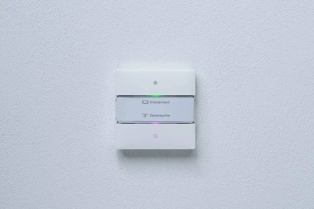 Przełącznik naścienny z dwoma przyciskami, oznaczony napisami 'Rozrywka' i 'Lampa sufitowa', każdy z małą lampką kontrolną.