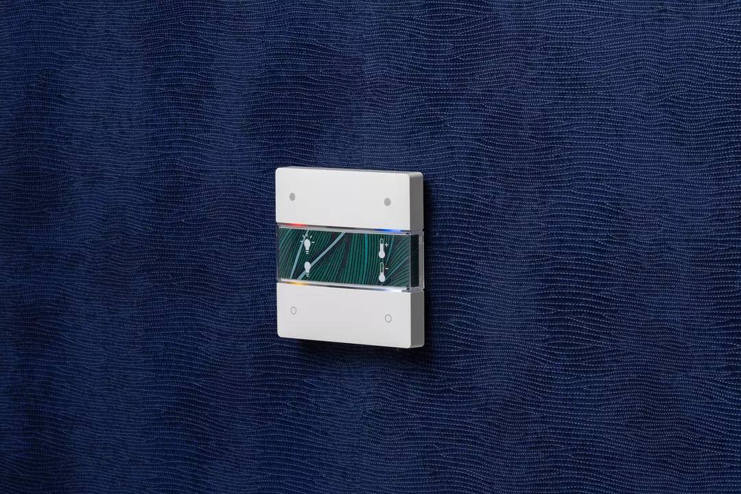 Biały, nowoczesny włącznik światła z elektronicznymi komponentami, zamontowany na ciemnoniebieskiej strukturalnej ścianie.