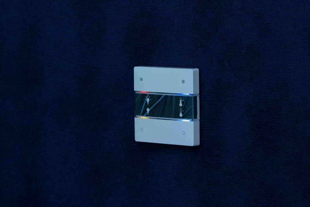 Elektroniczne urządzenie o gładkiej powierzchni z niebieskimi podświetleniami po bokach, zamontowane na ciemnoniebieskiej ścianie.