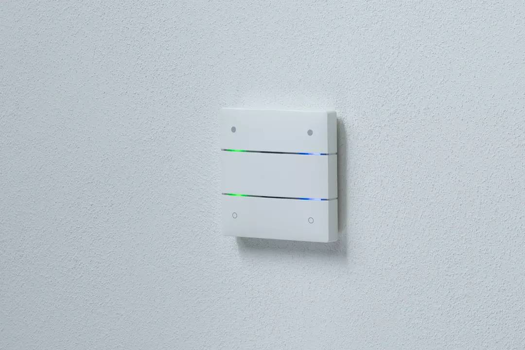 Elektroniczne urządzenie ścienne z dwoma świecącymi paskami LED w kolorach niebieskim i zielonym, zamontowane na białej ścianie.