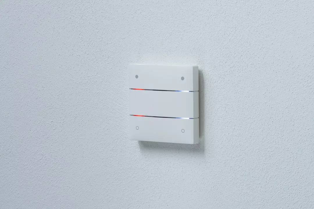 Nowoczesny biały włącznik ścienny z poziomymi paskami LED świecącymi na niebiesko i czerwono. Zamontowany na białej ścianie.