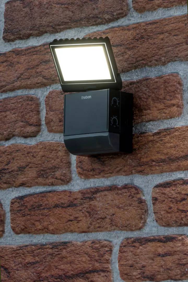 Czujnik ruchu z wbudowanym LED-owym reflektorem zamontowany na ścianie z cegły.