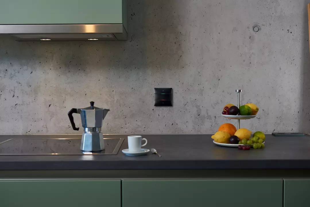 Kuchnia z szarym blatem, ekspres do espresso, filiżanka kawy, talerz z różnymi owocami. Prosta, nowoczesna aranżacja.