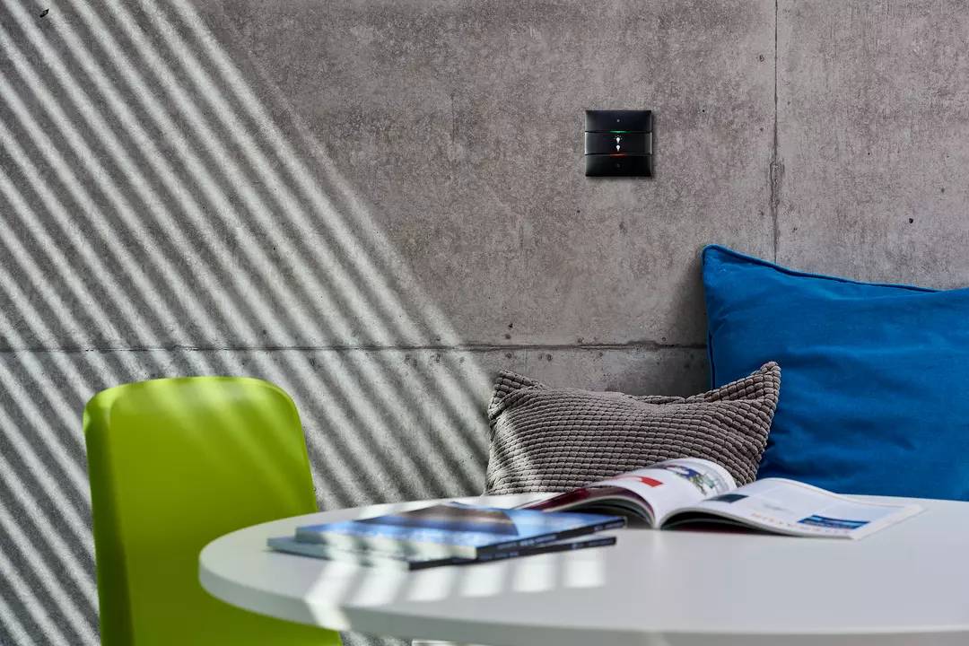 Okrągły stół z rozłożonymi magazynami i podświetlonym wzorem. W tle widoczna jest szara ściana betonowa, niebieska poduszka i zielone krzesło.