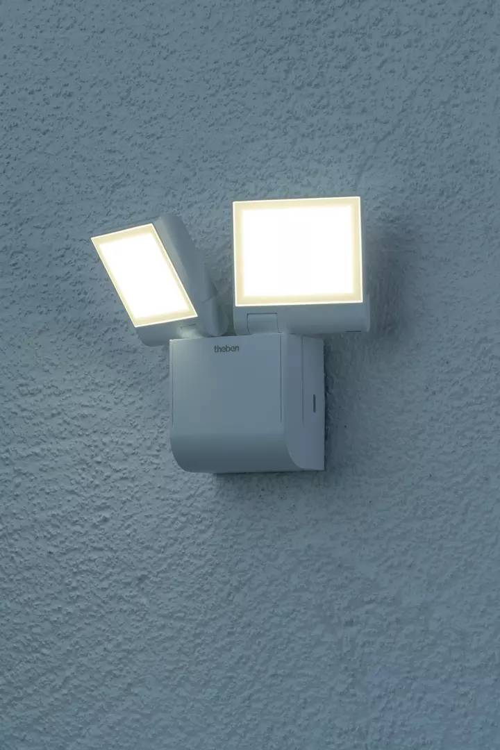 Podwójny kinkiet oświetla ścianę. Dwa kwadratowe źródła światła są jasne i skierowane w różnych kierunkach.