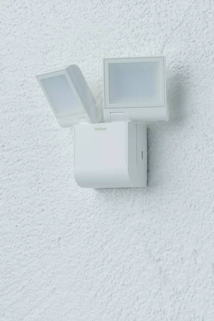 Biała lampa ścienna z czujnikiem ruchu, zamontowana na strukturalnej białej powierzchni.