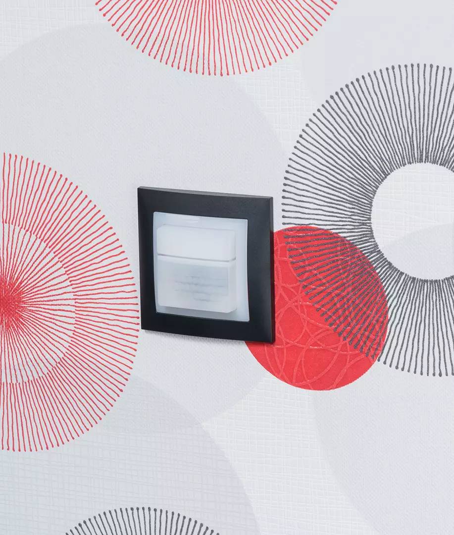 Czujnik ruchu na ścianie z czerwono-czarnym wzorem kołowym.