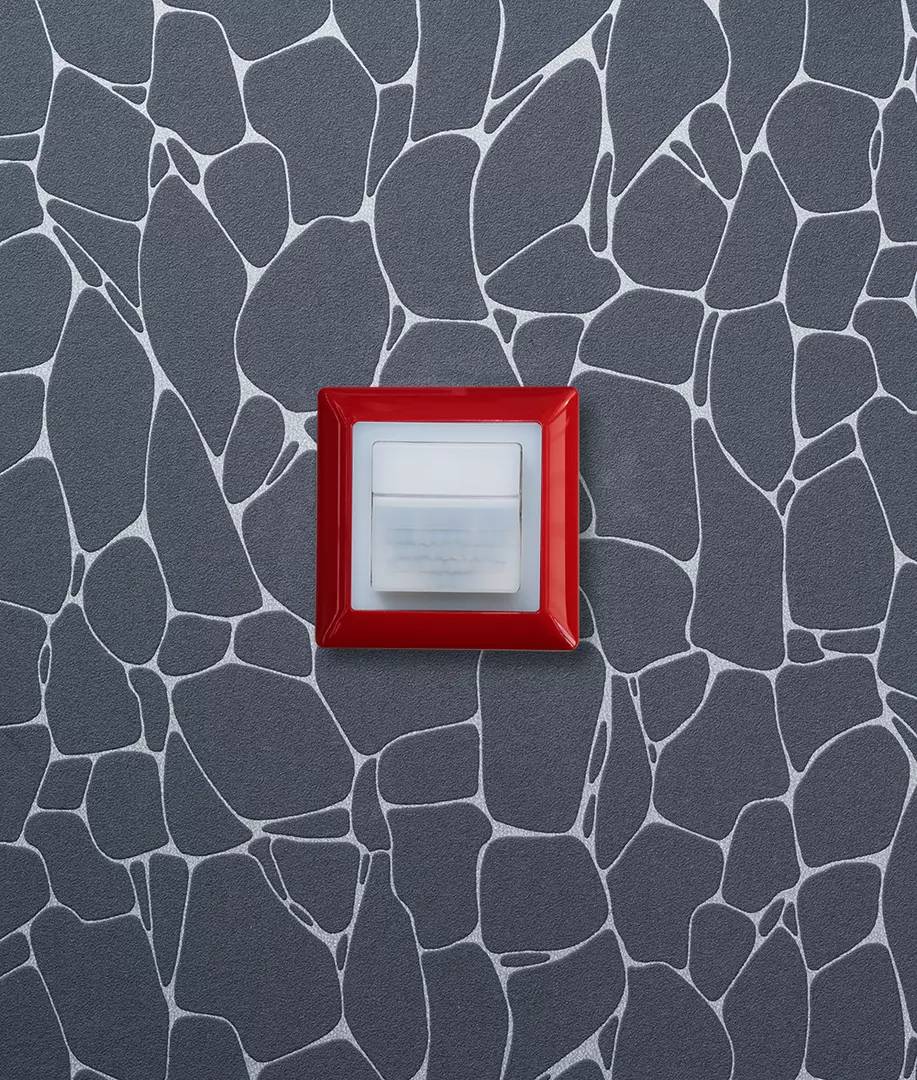Włącznik światła z czerwoną ramką na szarej ścianie z wzorem siatki.