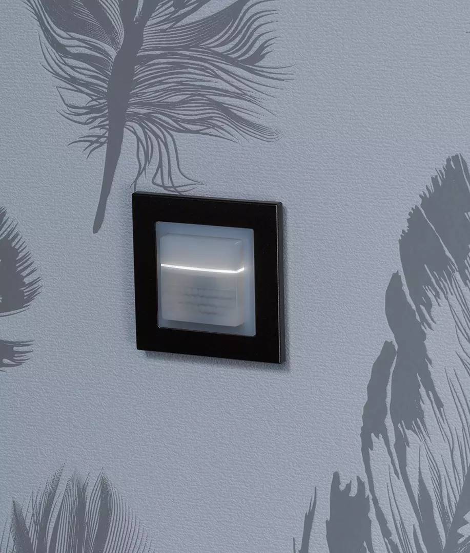 Kwadratowy, czarny włącznik światła jest wbudowany w ścianę o wzorze piór. Przełącznik świeci się w środku.