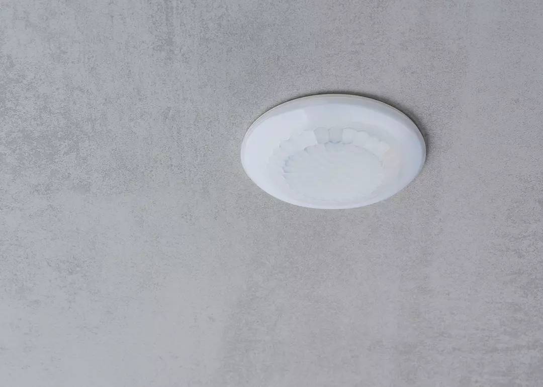 Lampa sufitowa, okrągła i biała, zamontowana na szarym suficie.