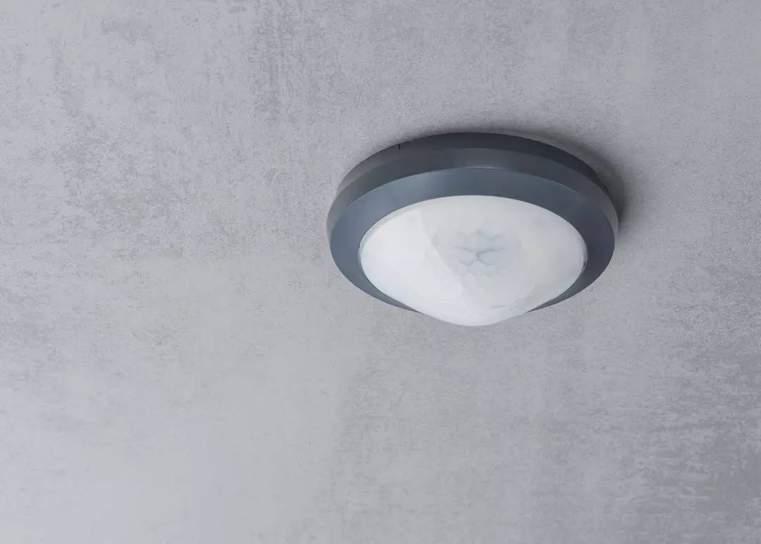 Okrągła lampa sufitowa z szarą ramką i białym kloszem, zamontowana na suficie pomieszczenia.