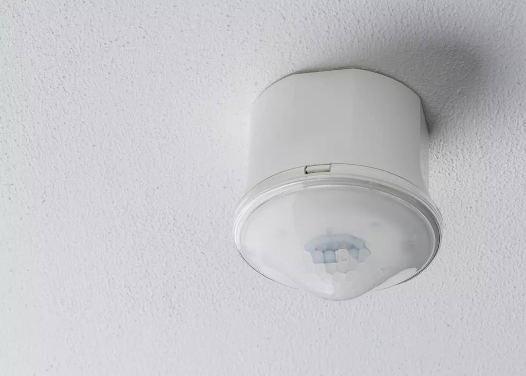 Okrągły czujnik ruchu jest zamontowany na białym suficie. Służy do wykrywania ruchów w pomieszczeniu.