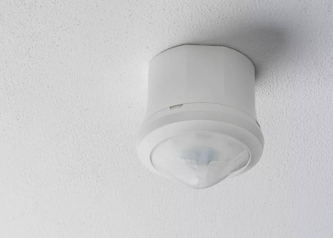 Sufitowy czujnik ruchu o okrągłym kształcie w białej obudowie.