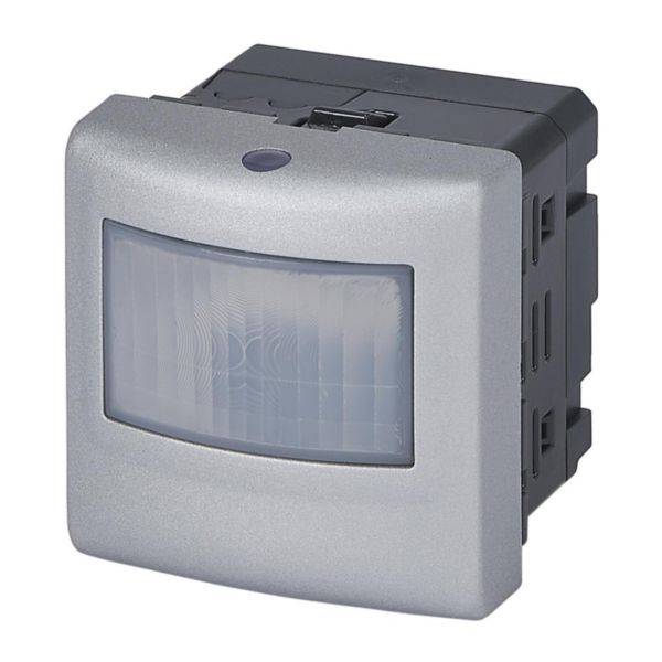 Srebrny czujnik ruchu w prostokątnej obudowie, przeznaczony do montażu naściennego wewnątrz pomieszczeń.