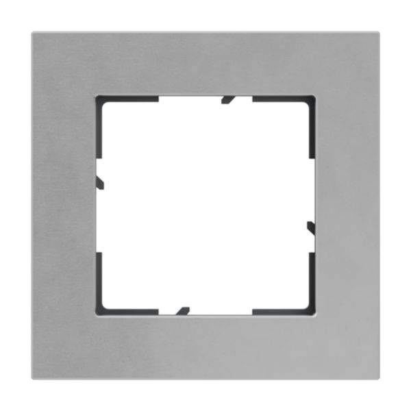 Srebrna, kwadratowa ramka z prostokątnym otworem pośrodku, prawdopodobnie przeznaczona do zamontowania włącznika światła lub gniazdka elektrycznego.