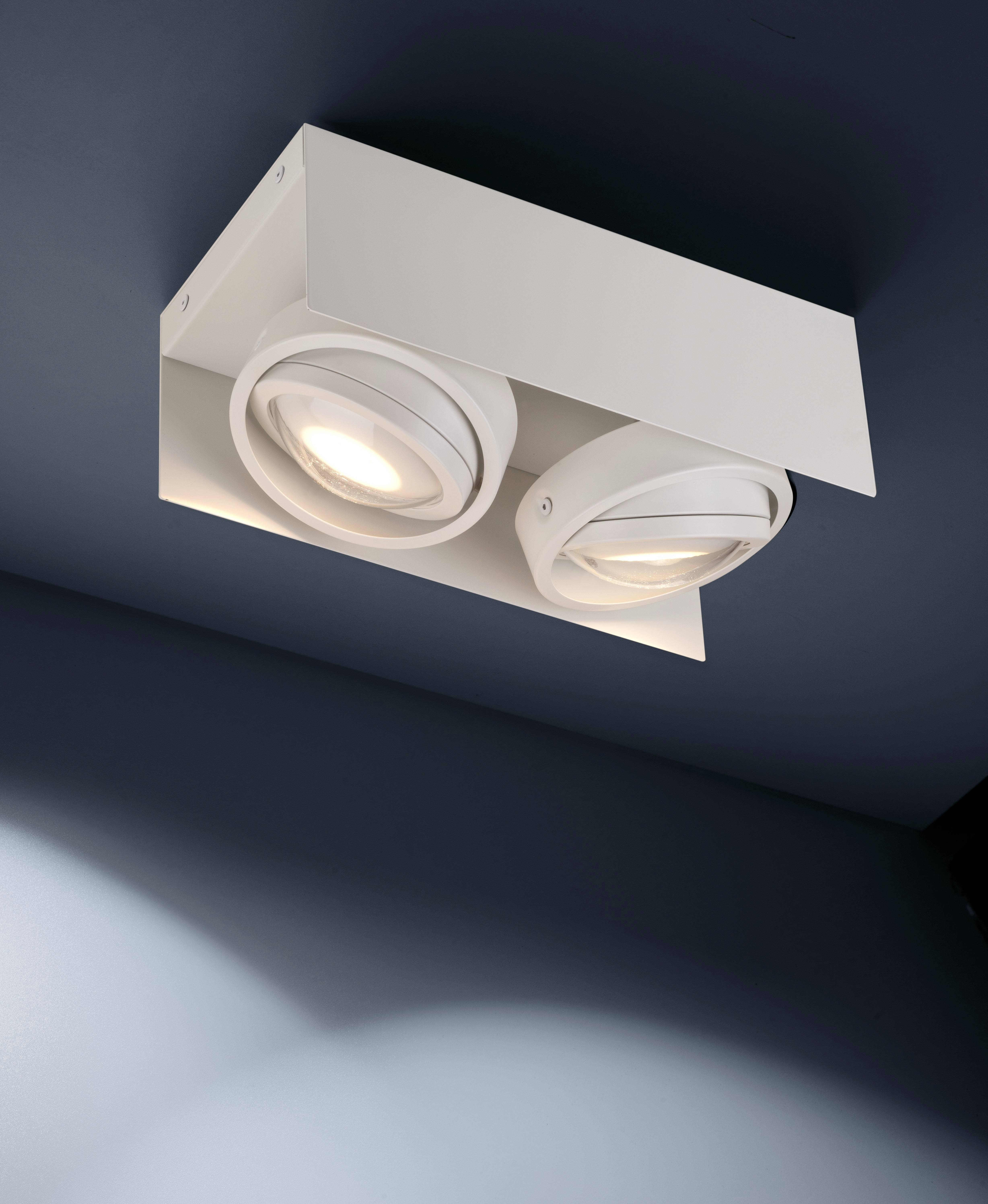 Dwa białe, nowoczesne reflektory sufitowe oświetlają pomieszczenie, zamontowane na ciemnym suficie.