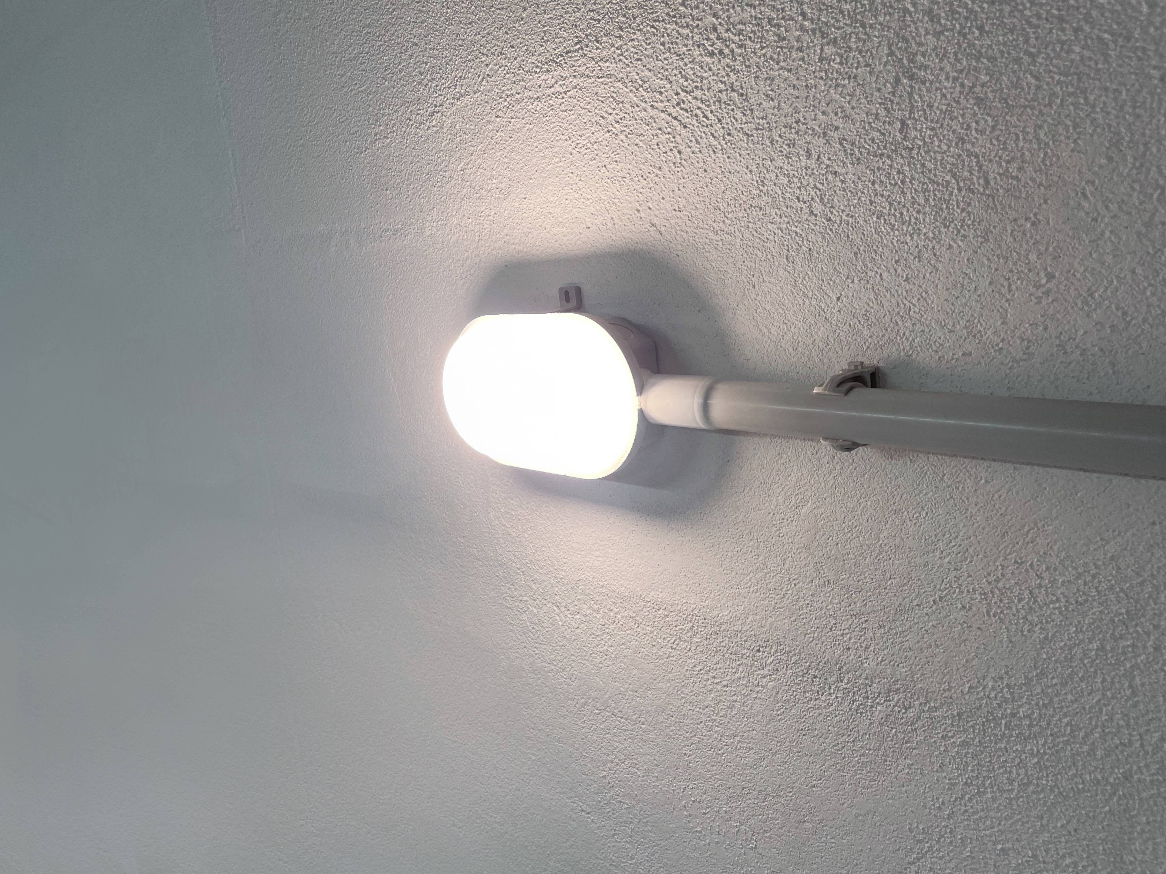 Świecąca lampa sufitowa z widoczną rurą, oświetlająca białe wnętrze.