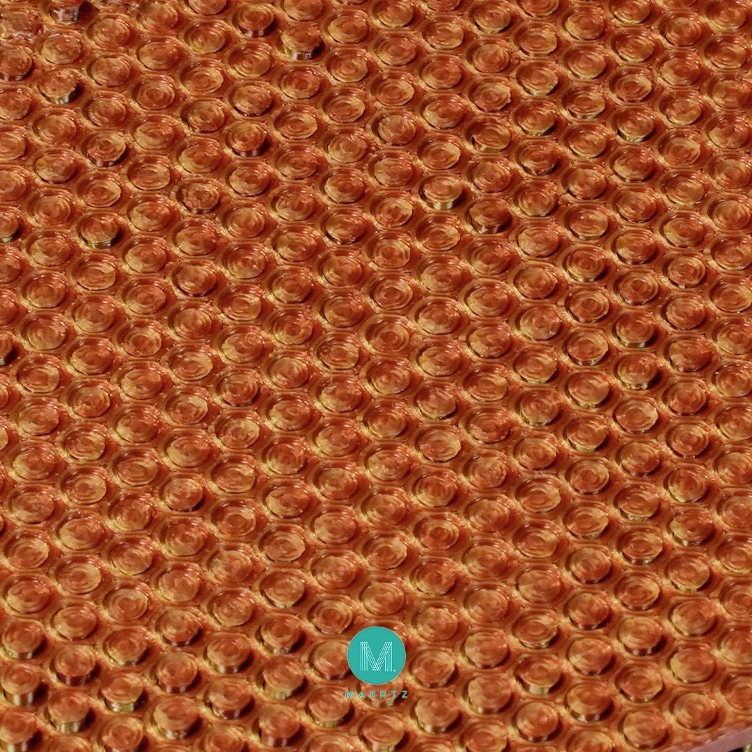 Zbliżenie na folię bąbelkową z gęsto upakowanymi pomarańczowymi bąbelkami. W dolnej części widnieje niebieskie logo z literą 'M'.