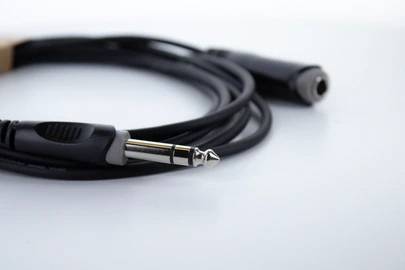 Czarny kabel audio z wtyczką jack 6,35 mm i gniazdem, leżący na białej powierzchni.