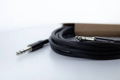 Czarny kabel audio z dwoma wtyczkami jack 6,3 mm po obu stronach, częściowo zwinięty, na białym tle.
