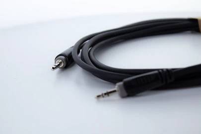 Czarny kabel audio z dwoma wtyczkami jack 3,5 mm leży na białym tle.