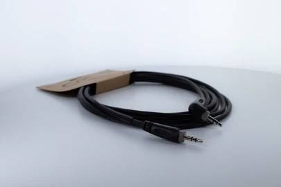 Czarny kabel audio z wtyczkami 3,5 mm na obu końcach, leżący na szarym tle.