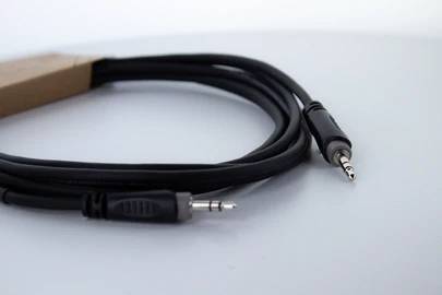 Czarny kabel audio z wtyczkami jack 3,5 mm na obu końcach leży na szarej powierzchni.