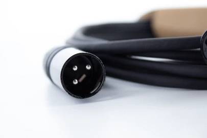 Przewód XLR z trzema pinami jest zwinięty na białej powierzchni. Jest często stosowany do połączeń audio.