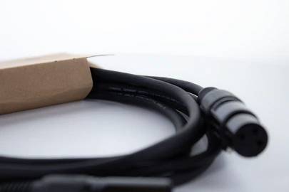 Czarny kabel audio z wtyczką XLR leży na powierzchni. Kawałek kartonu częściowo zakrywa kabel.