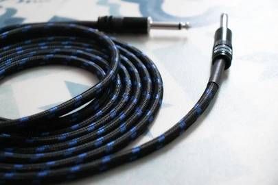 Kabel audio z czarno-niebieskim oplotem, ukazujące wtyk jack oraz szczegóły połączenia. Leży na niebieskim tle.