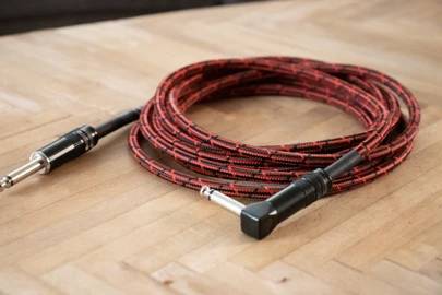 Czerwono-czarny pleciony kabel audio z prostą i kątową wtyczką jack 6,35 mm leży na drewnianym stole.