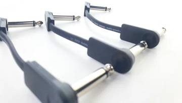 Trzy czarne kable łączące do efektów gitarowych z wtykami jack 6,35 mm leżą na białej powierzchni.