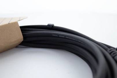 Czarny, zwinięty kabel wystaje z brązowego kartonu. Znajduje się na białej powierzchni.